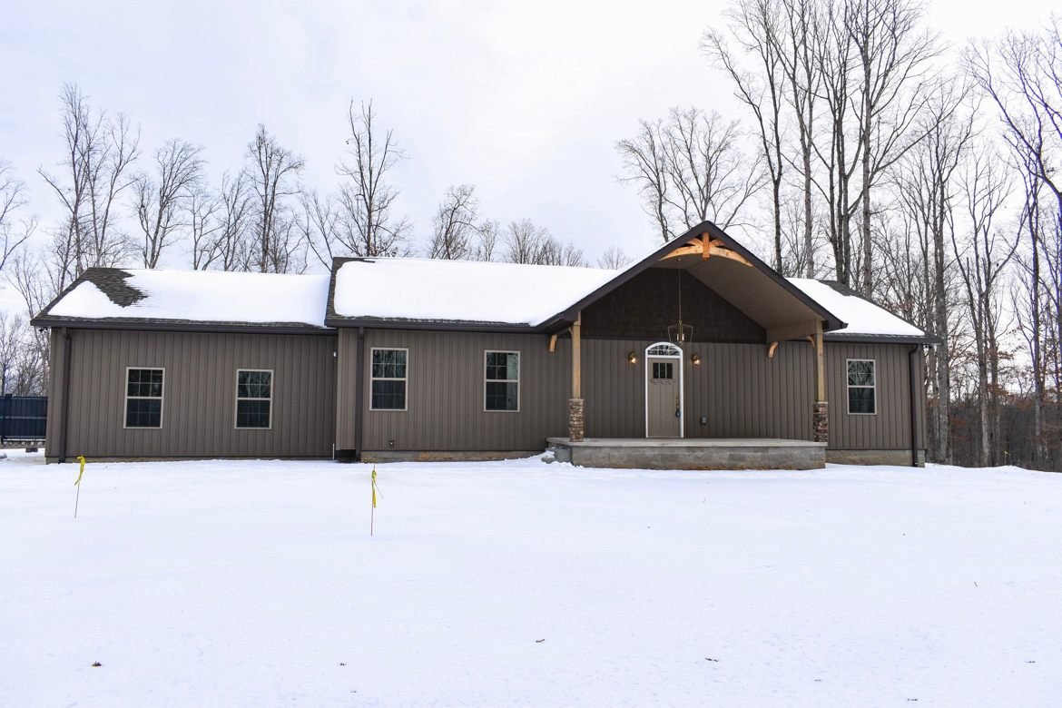 Finished home with a timber-frame gable entry and stone-based porch posts, standing in winter snow