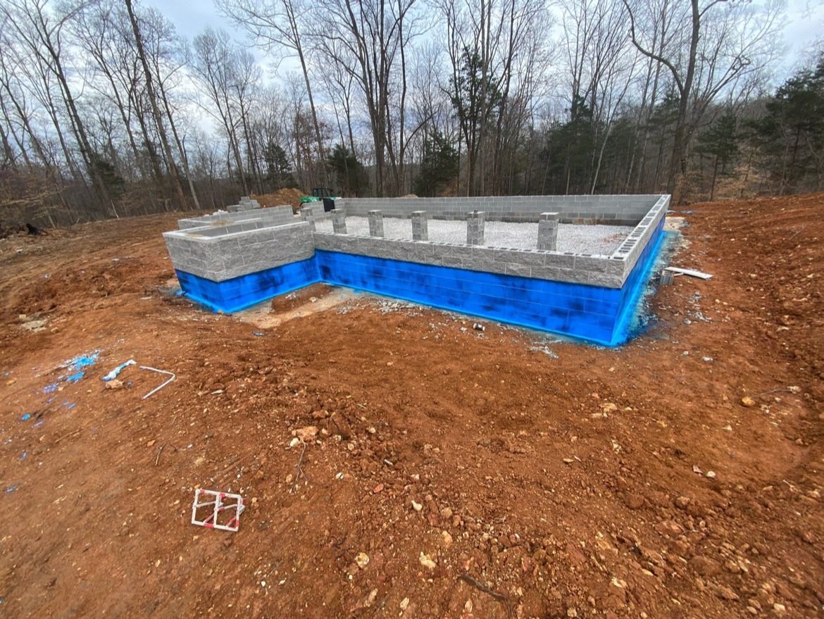 Concrete block foundation walls with blue waterproof membrane, set on a cleared red-clay lot