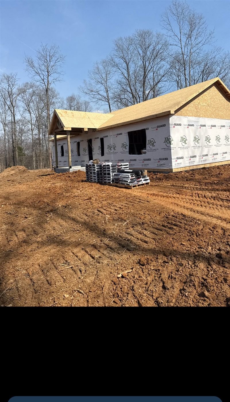 Framed house shell wrapped in OSB sheathing and house wrap, with a timber-frame porch gable taking shape