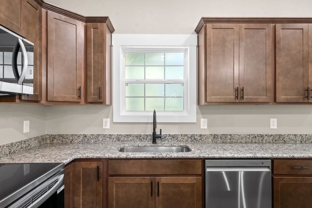 Kitchen with stained-wood cabinets, granite counters, a window over the sink and a stainless dishwasher in a new-construction home