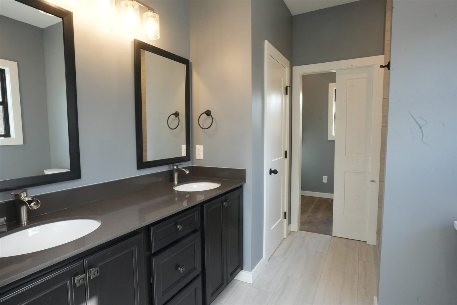 Bathroom with a long double vanity in dark cabinetry, a charcoal countertop and two black-framed mirrors