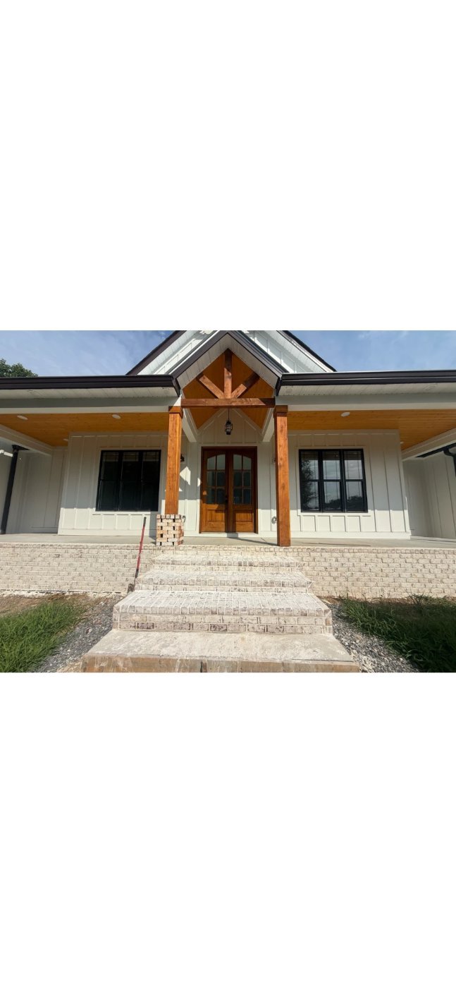 Front entry with a timber-frame gable over double wood doors, board-formed siding, black-framed windows and brick steps